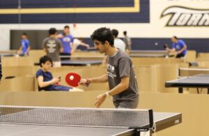 A teenager playing ping pong, with paddle in hand ready to hit a ball across a ping pong table