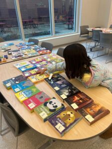 Child leaning over a table covered with books and reaching